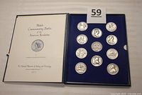 Opened presentation case showing 11 round pewter medals displayed in blue velvet lining, with fronts and backs visible.