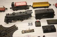 Photo of the locomotive, tender, dump car with red bin, yellow barrel car, track pieces, and controllers on display surface.