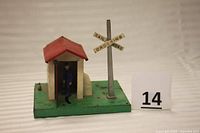 Front and side view of the vintage O gauge railroad crossing, showing the gatehouse with a red roof, the blue-clad gateman figure, and railroad crossing sign.