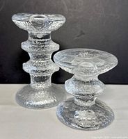 Two clear textured glass candle holders of different heights with organic rippled surface pattern on a white surface with black background.