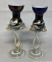Front view of two iridescent polychrome glass candlesticks with twisted threaded feet and wide bases with white rings.