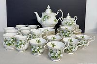 Front view of full tea set arranged with cups, plates, teapot, sugar bowl, and creamer