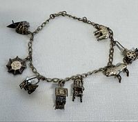 Full view of the silver charm bracelet showing all attached miniature charms including the sailboat, horse-drawn carriage, hand, umbrella, pagoda, chair, and ornate hexagonal charm.