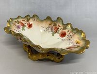 Side view of antique Moore Bros footed bowl showing scalloped gold-trimmed rim and floral pattern over white porcelain with ornate gold footed base.