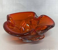 Orange art glass bowl with wavy edges from an angled side view, showing thickness and clear base