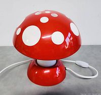 Front view of the red mushroom shaped lamp with white spots, showing the power cord and switch.