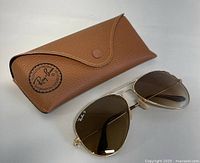 Photo of brown textured leather Ray-Ban case with snap button and sunglasses laid beside it