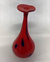 Front view of red hand blown glass vase with blue spots showing bulbous base and flared neck.