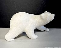 Side view of white marble polar bear sculpture showing walking posture and body contours.