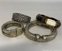 Four vintage hand-crafted bangles displayed side by side, showing detailed textures and designs on each piece.