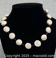 Front view of conch shell necklace on black display stand, showing round shell beads and silver clasp at ends.
