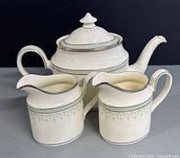 Front angled view of vintage English PORTLAND by Minton bone china tea/coffee pot with two matching creamers showing the spout, handles, lid, and decorative pattern.