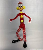 Front view of the vintage Murano glass clown figurine showing details including facial features, yellow cheeks and buttons, red hat and body, and swirl pattern on legs.