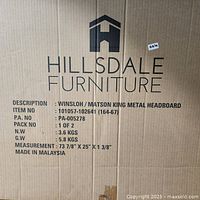 Close-up photo of cardboard box with Hillsdale Furniture logo and product info label showing Winsloh/Matson King Metal Headboard, dimensions, weight, and origin.