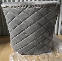 Rear view of gray tufted chair top with quilted diamond pattern and silver nailhead trim along the top edge.