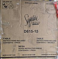 Image of cardboard packaging box with Signature Design Ashley branding, model number D615-15. Box is torn with shipping damage visible.
