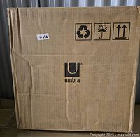 Closed cardboard box labeled with Umbra logo containing the new Umbra Triflora Hanging Planters.