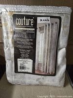 Packaged curtain panel with label showing brand, size, material, care instructions, and a photo of the curtain hanging.