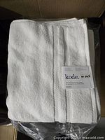 Folded white Turkish cotton bath towel with Kode brand tag on top, showing towel texture and packaging beneath.