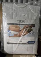 Front view of packaged Millano mattress pad showing product label and branding.