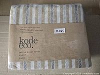 Folded Kode Eco Terran duvet cover wrapped in brown paper label, showing striped fabric pattern in beige, white, and black.