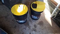Two black 5-gallon Home Depot Pro XTREME buckets with closed yellow lids, placed on a concrete floor.