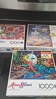 Photo of three sealed 1000-piece jigsaw puzzle boxes featuring colorful fantasy artwork by Aimee Stewart and Josephine Wall with billboard reductions.