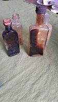 All four antique glass bottles on green fabric surface showing varied sizes and color