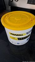 Front view of Frabill 4.5 qt white bait bucket with yellow ventilated lid on a black surface