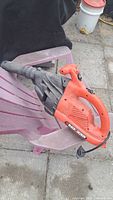 Photo of orange and black Black and Decker electric leaf blower on a purple plastic chair, showing the nozzle and handle with power cord
