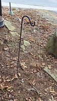 Smaller single-hook metal garden stake in the ground surrounded by soil and dried leaves.