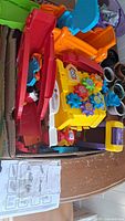 Box containing colorful track pieces including red and yellow tracks, an activity box with gears, and toy car parts.