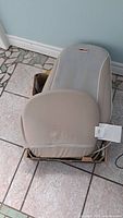 Obusforme heated chair cushion resting in cardboard box on tiled floor showing full gray mesh backrest and beige cushioned seat.