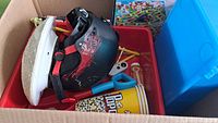 Box containing items including a black ski helmet, toy shovel, popcorn holders, Candy Land board game, and bubble toys.
