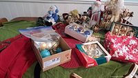 Wide view of table showing multiple Christmas decorations and boxes of ornaments, along with various figurines and textiles.