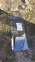 Full view of rectangular metal live trap cage placed on grass surface