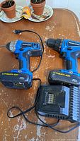 Photo showing two Mastercraft cordless drills, two 20V lithium-ion batteries attached, and a charger on a wooden surface.
