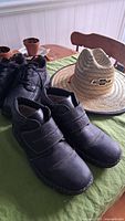 Two pairs of men's black leather shoes and a beige and black Chevrolet branded straw hat on a green cloth-covered table