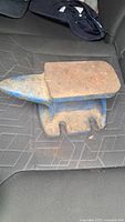 Top and side views of a small blue metal anvil with rust and wear visible, placed on a car seat.