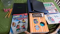 Photo showing curriculum books, a math workbook, and binders on a green surface.