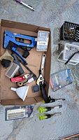 Full view of assorted hand tools and accessories on a cardboard surface outdoors.