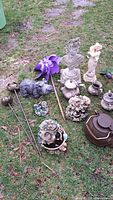 Overview of 13 garden decor items on grass including statues, teapots, wind spinner and floral candle holders.