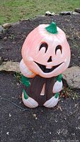 Front view of the vintage blowmold Halloween pumpkin decoration placed on gravel outdoors.