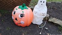 Photo showing the full vintage blow mold pumpkin and ghost Halloween decorations side by side outdoors on grass and soil.