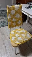 Full view of vintage kitchen chair showing yellow vinyl seat and backrest with white floral pattern, chrome legs and decorative top bar.