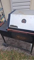 Right-side view of the smoker showing the white lid with Traeger logo and black metal body. Rust visible on lower black metal section.