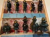 Top view of all 10 carbide router bits set in wooden case with bubble wrap lining. Each bit has a black body with brass-colored top and silver shank.