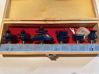 Wooden case with 6 blue metal router bits arranged inside, includes label describing bit types and uses.