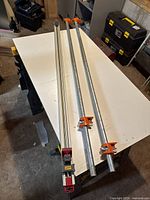 Three metal pipe clamps on a table; two orange-headed pipe clamps and one red/silver Gator Clamp