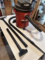 View of red Genie wet/dry vacuum with black hose connected, showing body and accessories laid out on a table